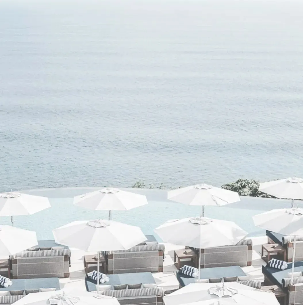 Rows of white umbrellas and daybeds on a clifftop terrace above the ocean at Savaya.