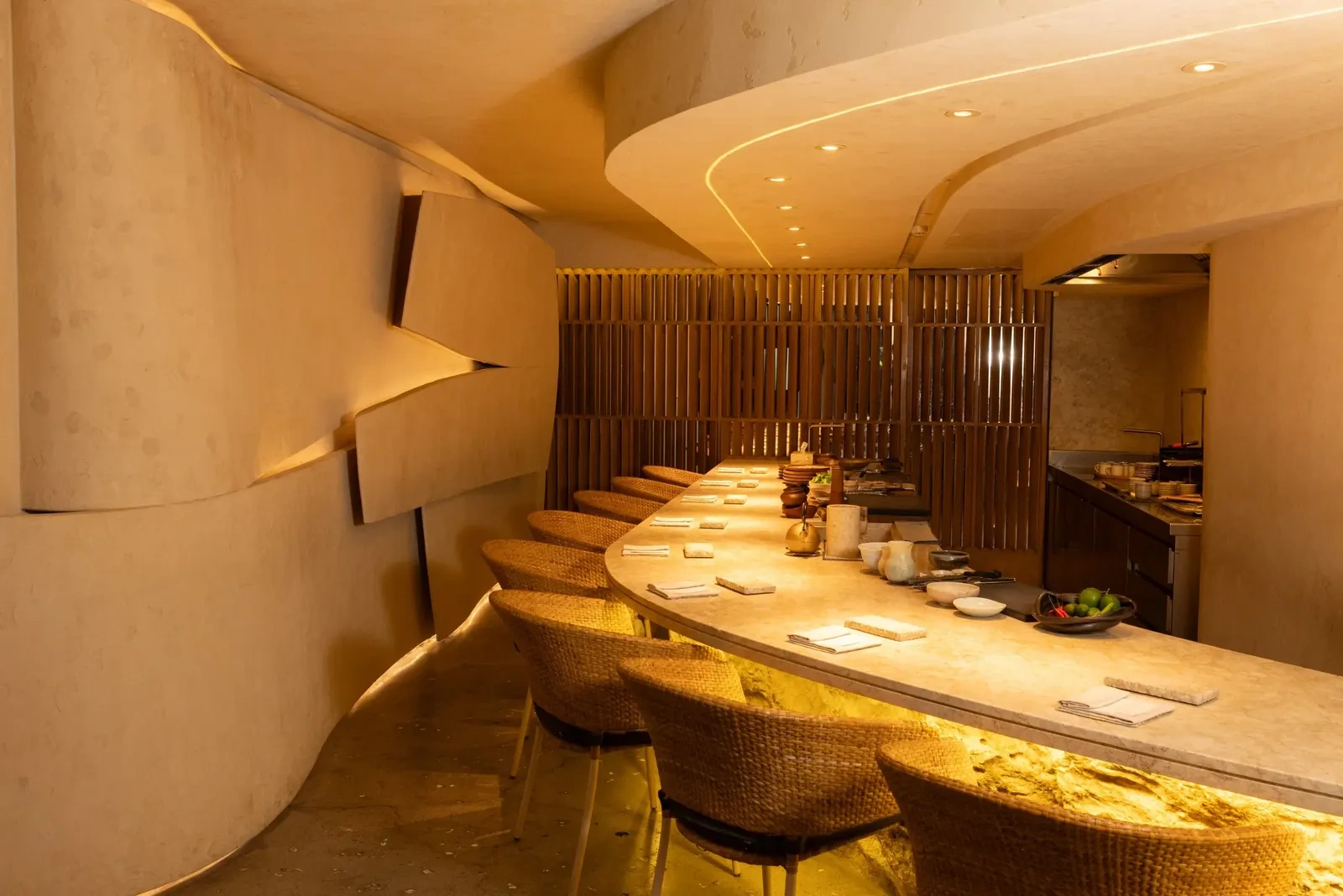 A curved, softly lit dining room with a long pale counter and rattan chairs at Inatô in Makati.