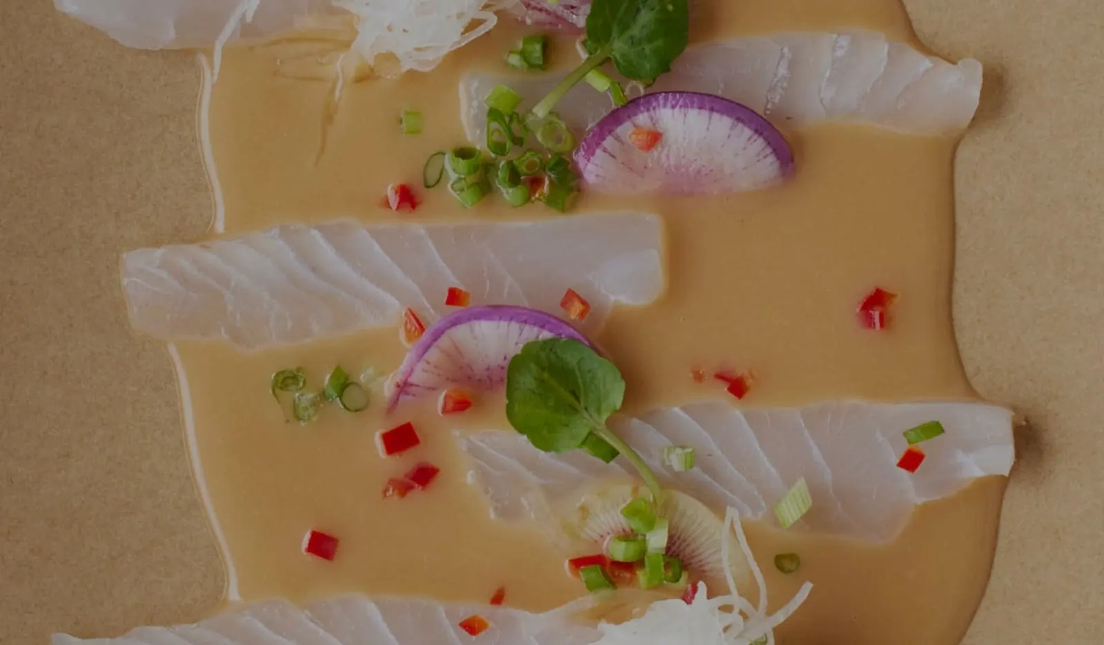 Slices of raw white fish in a golden dressing with radish, spring onion and chilli at Pica.