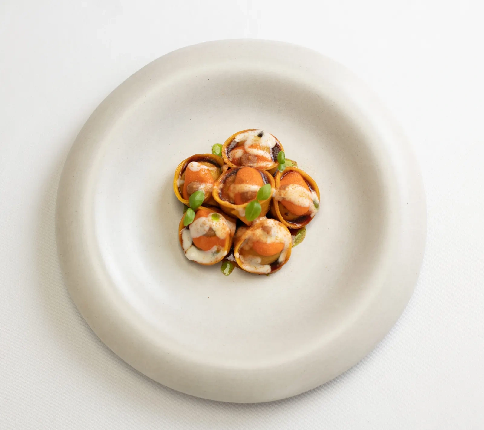 A small ring of filled pasta in an orange sauce with green herbs, centred on a wide white plate at MAURI.