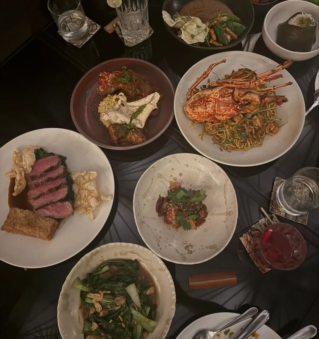 A table of shared Indonesian dishes seen from above at Merah Putih, including sliced beef, a lobster with noodles, greens and small plates.